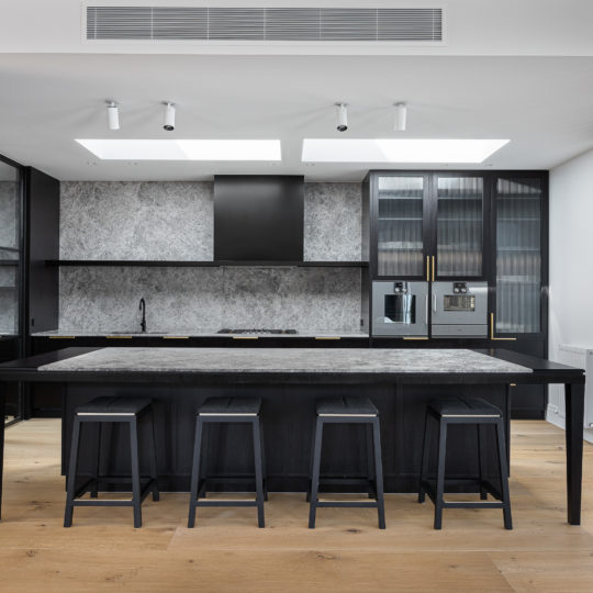 A beautiful kitchen with elegant timber flooring, dark joinery and grey stone