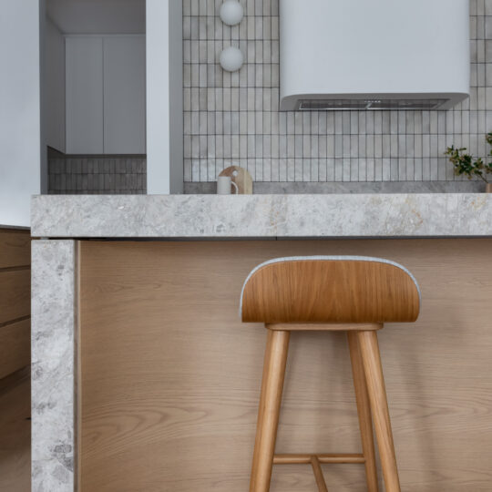 A modern kitchen featuring a curved application of Cellupal Eik oak-look laminate beneath the grey stone-topped island bench.