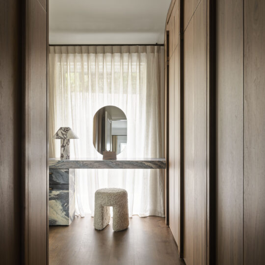 A beautifully designed dressing area at Finch House, featuring floor-to-ceiling joinery crafted from Lignapal walnut veneer panels. Natural light filters through soft curtains, highlighting the warm tones of the timber and a striking marble vanity